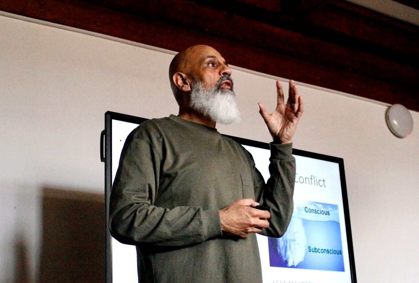 Mubeen Azam speaking with a slide on conflict behind him, Truro